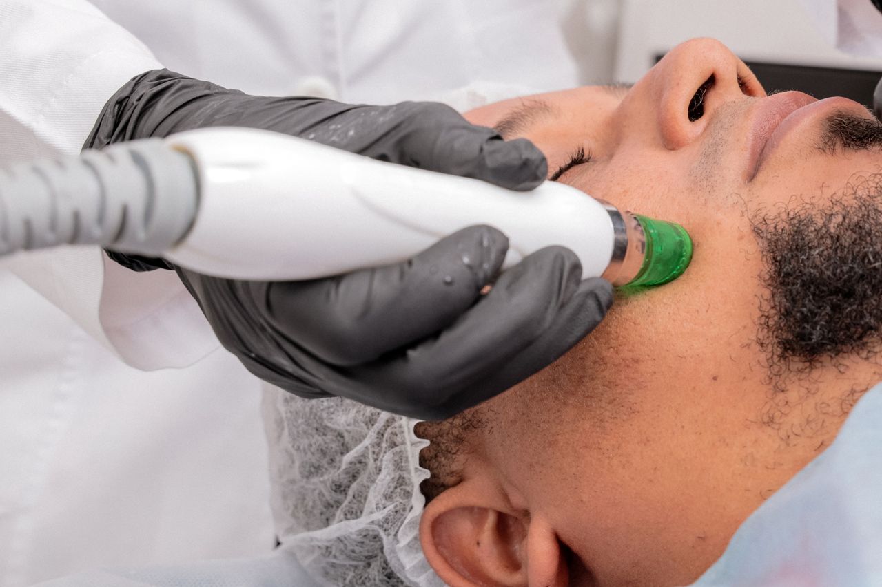 Home A close-up of a man receiving a professional skincare treatment in a clinical setting.